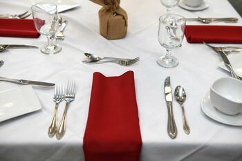 Photo of table place settings with silverware and red napkins on a white tablecloth